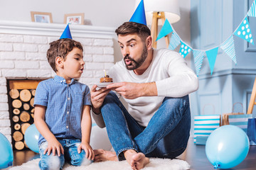 Do it quickly. Positive delighted daddy blowing out candle, sitting near his son