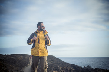 Male trekker walking and enjoying the nature on the coastline in a vulcanic island. ocean and desert around him. travel alone and discover places concept. blue tones for cold day