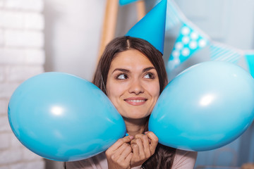 Happy woman. Charming brunette keeping smile on her face and holding balloons in both hands