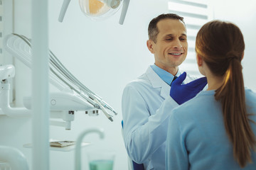 Teeth examination. Handsome doctor keeping smile on face while treating his friend