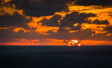 Fototapeta premium The sun, hidden by clouds, descends into the sea