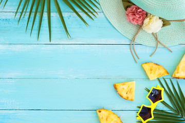 Holidays concept. Palm leaves, straw hat, pineapple slices and sunglasses on wood plank blue color. Summer vacation background concept. top view