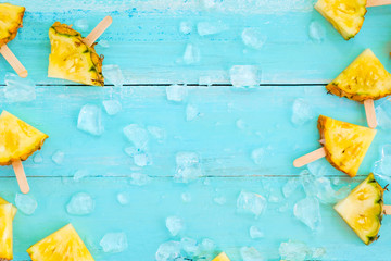 Slices pineapple popsicle sticks with ice on wood plank blue color. summer fruit backgrond concept, top view, copy space