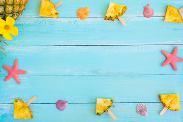 Summer concept. Frame made of pineapple popsicle sticks, starfish and shells on wood plank blue color. vacation background. top view
