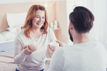 Fototapeta premium New cups. Cheerful young emotional coupe sitting at home and smiling while holding their new beautiful cups