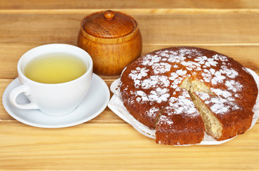 Homemade cake decorated with powdered sugar and a cup of green tea on a wooden table