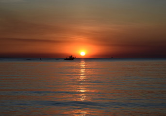 Obraz premium A cruising sail boat passes majestically beneath the enchanting sunset. The Sun casts orange shades across an evening sky at Mindil Beach (Darwin, Northern Territory, Australia).