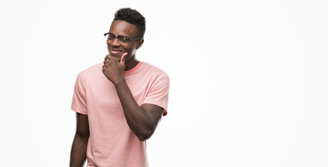 Young african american man wearing pink t-shirt looking confident at the camera with smile with crossed arms and hand raised on chin. Thinking positive.