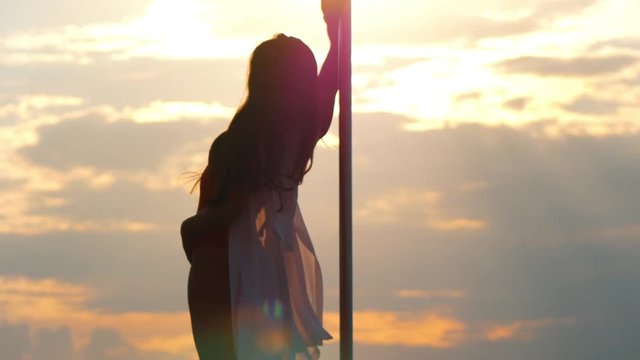 Sexy woman performs pole-dance against the sunset outdoors