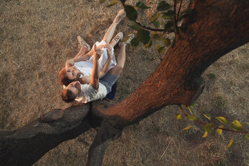 A loving couple is sitting under a tree. A guy and a girl embrace in the open air at dawn in the summer.