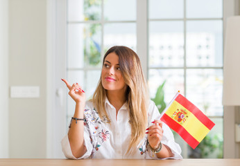 Young woman at home holding flag of Spain very happy pointing with hand and finger to the side