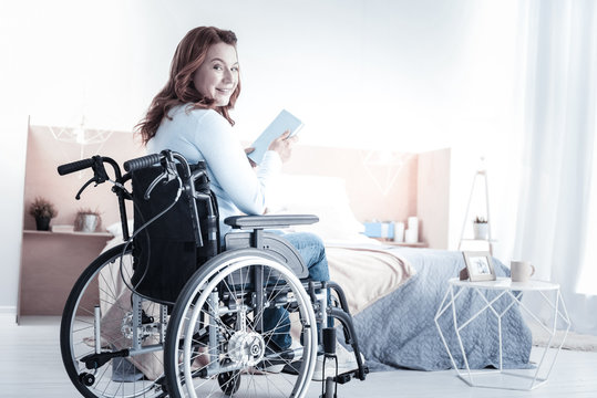 Time with pleasure. Charming brunette keeping smile on her face while sitting on wheelchair