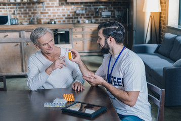 Effective pills. Good-looking cheerful young man smiling and holding some pills while talking with...