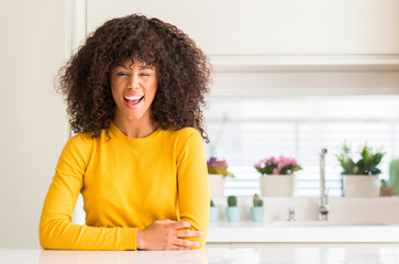 African american woman wearing yellow sweater at kitchen winking looking at the camera with sexy expression, cheerful and happy face.