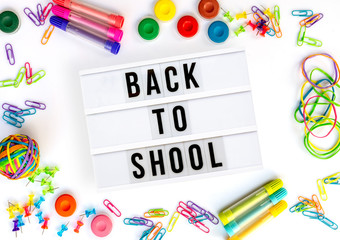 Back to school written in a light box, colorful school supplies isolated on white
