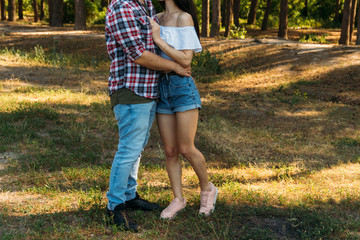 embrace.Love and affection between a young couple at the park. a guy in a plaid plane and jeans, a girl in shorts and a white jacket. They get together in the forest for a walk.
