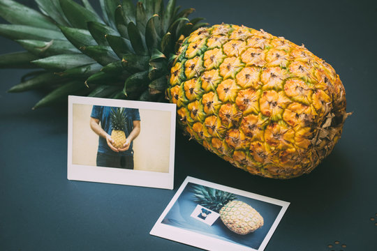 Juicy pineapple with two instant photos on a black table, outdoors.