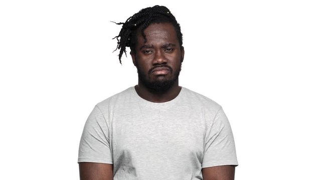 Portrait of displeased dark skinned guy in casual t-shirt with afro pigtails shaking head in denial or expressing dislike, isolated over white background slow motion. Concept of emotions