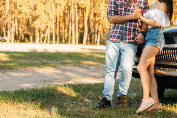 embrace.Love and affection between a young couple at the park, near the old car. a guy in a plaid plane and jeans, a girl in shorts and a white jacket. They get together in the forest for a walk.