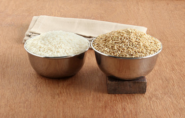 White rice and brown rice in steel bowls. Brown rice is said to be a healthier food than its white counterpart, because of high fiber, magnesium and antioxidant and other useful elements.