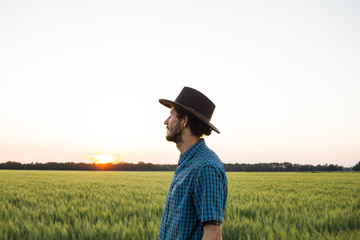 YOung male farmer stand alone in wheat field during sunset 