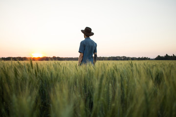 Naklejka na ściany i meble YOung male farmer stand alone in wheat field during sunset 