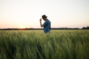 Naklejka na ściany i meble YOung male farmer stand alone in wheat field during sunset 