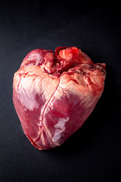 Beef raw heart on a black background with rosemary and spices.