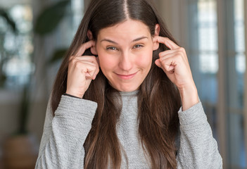 Young beautiful woman at home covering ears with fingers with annoyed expression for the noise of loud music. Deaf concept.