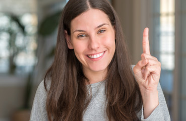 Young beautiful woman at home showing and pointing up with finger number one while smiling confident and happy.