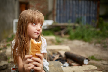 Portrait of hungry homeless girl eating a piece of bread in the dirty alley
