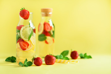 Fresh fruit flavored water with strawberry, lemon, mint on yellow background. Summer drink concept. Copy space. Infused water or citrus lemonade