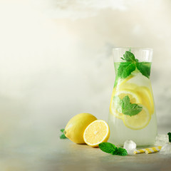 Citrus lemonade - mint, lemon and tropical monstera leaves on grey background. Square crop. Detox drink. Summer fruit infused water. Copy space.
