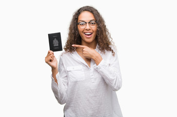 Young hispanic woman holding passport of Canada very happy pointing with hand and finger