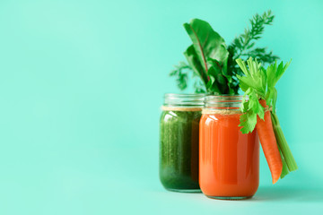 Healthy organic green and orange smoothies on blue background. Detox drinks in glass jar from vegetables - carrot, celery, beet greens and tops. Copy space. Summer food concept