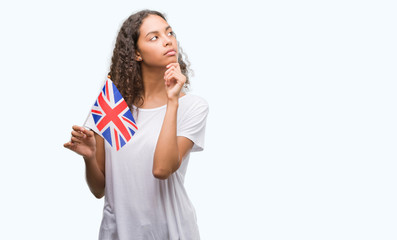 Young hispanic woman holding flag of United Kingdom serious face thinking about question, very confused idea