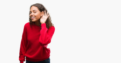 Young hispanic woman wearing red sweater smiling with hand over ear listening an hearing to rumor...