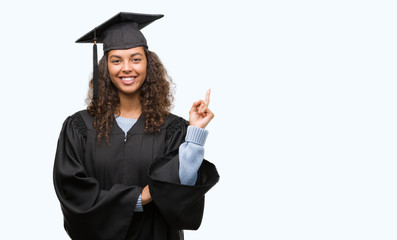 Young hispanic woman wearing graduation uniform very happy pointing with hand and finger to the side