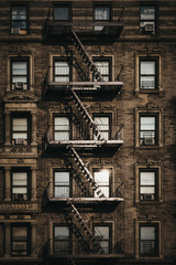 Facade of a typical New York block of flats with fire escape at the front, sun reflects in the windows.
