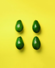 Green avocado pattern on yellow background. Top view. Pop art design, creative summer food concept. Organic avocadoes in minimal flat lay style.