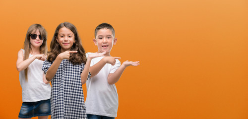 Group of boy and girls kids over orange background very happy pointing with hand and finger