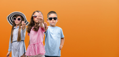 Group of boy and girls kids over orange background with open hand doing stop sign with serious and...
