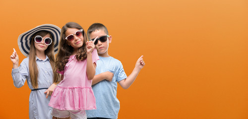 Group of boy and girls kids over orange background very happy pointing with hand and finger to the...