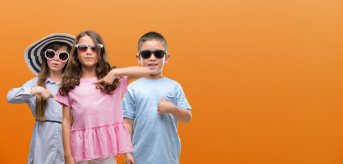 Group of boy and girls kids over orange background with surprise face pointing finger to himself