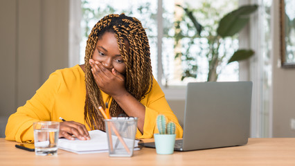 African american woman studying with laptop cover mouth with hand shocked with shame for mistake, expression of fear, scared in silence, secret concept