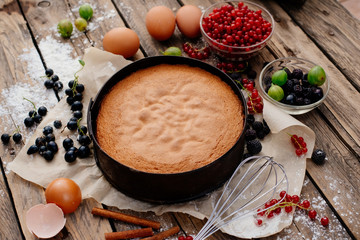 Process of preparation of biscuit with forest berries. Sponge cake. Biscuit strewn with berries and rubbed with powdered sugar on a wooden table. Country food.
