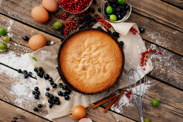 Process of preparation of biscuit with forest berries. Sponge cake. Biscuit strewn with berries and rubbed with powdered sugar on a wooden table. Country food.