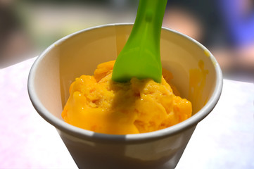Scoop of mango ice cream in paper cup with plastic spoon
