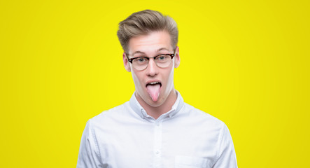 Young handsome blond man sticking tongue out happy with funny expression. Emotion concept.