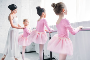 cute little kids in tutu skirts exercising with teacher in ballet school